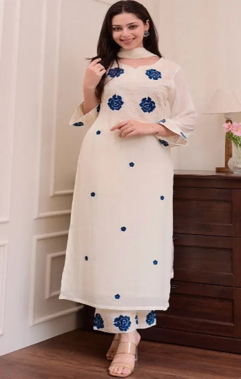 Woman wearing a white kurta with blue floral embroidery in a room setting.