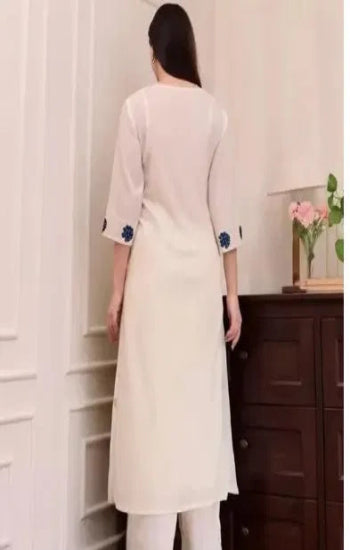 Woman wearing a white kurta with floral embroidery in a room.