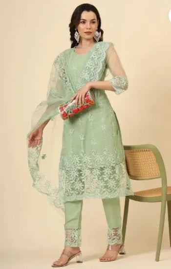Woman in a light green embroidered outfit holding a clutch against a beige background